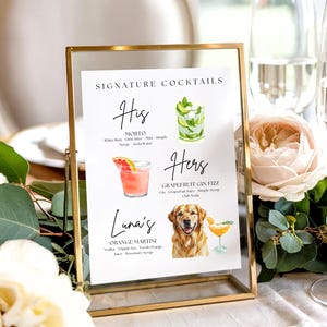 May include: A gold framed sign displays a cocktail menu with watercolor illustrations. The menu includes a Mojito, a Grapefruit Gin Fizz, and an Orange Martini. The sign is surrounded by flowers and glasses of champagne.