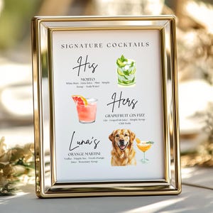 May include: A framed sign with gold trim displays a list of signature cocktails. The sign includes watercolor illustrations of a Mojito, a Grapefruit Gin Fizz, and an Orange Martini. The sign is labeled "Signature Cocktails" at the top.
