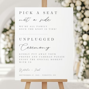 May include: A white wedding sign on a wooden easel with black text. The sign reads "Pick a seat, not a side," and "Unplugged Ceremony." The sign also includes the names Natalie & Josh and the date September 27, 2025, Toronto, ON.