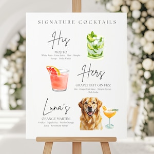 May include: A white sign on a wooden easel displays signature cocktail recipes. The sign features watercolor illustrations of cocktails and a golden retriever. The cocktails include a Mojito, Grapefruit Gin Fizz, and Orange Martini.