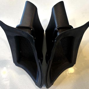 May include: Two matte black automotive air intake scoops featuring a wide, flared opening and a recessed hexagonal honeycomb mesh grille. Each unit has a tapered, angular body with visible mounting points along the inner frame edges.