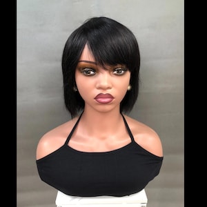 May include: A mannequin head with a short, black wig featuring bangs. The mannequin is wearing a black halter top. The face has makeup, including eye shadow and lipstick. The mannequin has gold star-shaped earrings.