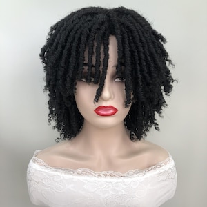 May include: A black, short-length wig with dreadlock-style curls. The wig is styled with a fringe that partially covers the forehead. The mannequin is wearing a white, off-the-shoulder top with lace detailing.