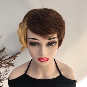 May include: A mannequin head with a short, two-toned wig. The wig features dark brown hair on top and a section of blonde hair on the side. The mannequin is wearing a black halter top and has red lipstick.