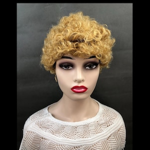 May include: A mannequin head wearing a short, curly, light-blonde wig. The mannequin has dark eye makeup and red lipstick. The mannequin is wearing a white, open-weave sweater. The background is a solid, dark gray.