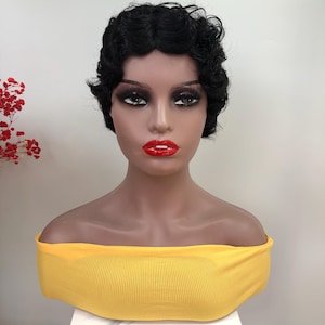 May include: A mannequin head with a short, black, wavy wig. The mannequin is wearing a yellow, off-the-shoulder top. The mannequin has red lipstick and dark eye makeup. The background is white.