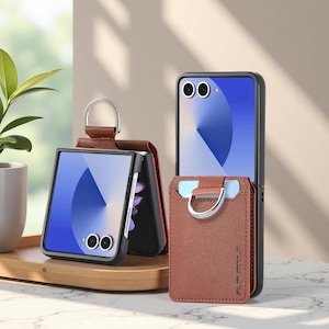 May include: A brown leather phone case with a silver ring and card holder is displayed next to a black phone case. The phone screens show a blue and white design. The cases are on a wooden tray.