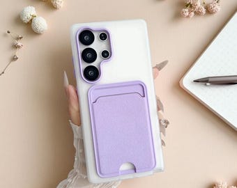 Puede incluir: Una funda transparente para teléfono con un tarjetero lila. La funda tiene un recorte para la cámara con detalles en morado. El tarjetero es rectangular con una parte superior curva y un recorte en la parte inferior.