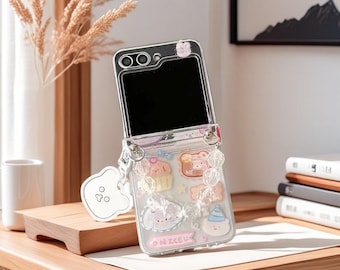 May include: Clear phone case with a hinged design, adorned with cartoon-style images of a bear, cupcake, and bunny. The case has a beaded strap and a white charm. The text "ONICEU" is visible on the case.