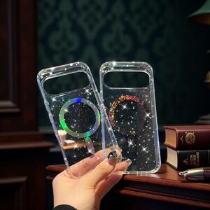 May include: Two clear phone cases with a sparkly design. One case has a rainbow-colored circle, and the other has a colorful, glittery circle. The cases are held by a person's hand. The cases are on a wooden surface.