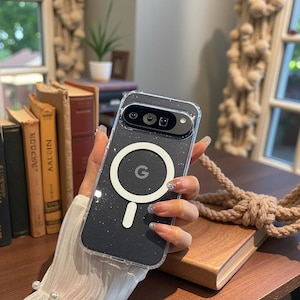 May include: Clear phone case with a black speckled design. The case has a white circular MagSafe charger with the Google "G" logo. The phone case is designed for a Google Pixel phone.