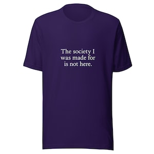 May include: A purple t-shirt with short sleeves and a crew neck. The white text on the front reads: "The society I was made for is not here." A comfortable, casual garment.
