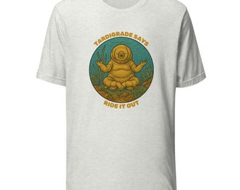 Puede incluir: Camiseta gris claro con un gráfico circular de un tardígrado en pose meditativa, rodeado de plantas acuáticas. El texto "Tardigrade Says Ride It Out" está arqueado arriba y abajo de la imagen en color amarillo-naranja.
