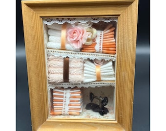 Vitrina en miniatura con temática de costura, marco de madera con detalles de encaje, estilo cottagecore.