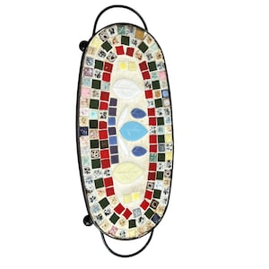May include: Oval mosaic tray with a black metal frame and handles. The mosaic features a floral design with red, blue, white, and yellow leaf shapes. The mosaic is made of small, colorful tiles.