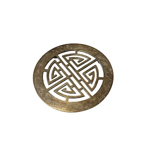 May include: A round, antique brass-colored decorative object with a central geometric design and floral border. The intricate pattern is cut out, creating negative space within the circle. The object is likely made of metal.