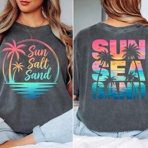 Puede incluir: Camiseta gris oscuro con un dise&ntilde;o colorido. En la parte delantera, "Sun Salt Sand" con palmeras y olas. En la espalda, "Sun Sea Sand" con palmeras y un atardecer, ideal para el verano y la playa.