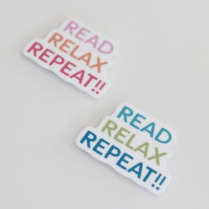 May include: Two stickers with the text "READ RELAX REPEAT!!" in a colorful gradient font. The stickers are white with a rounded edge. One sticker has a pink, orange, and red gradient, and the other has a blue, green, and blue gradient.