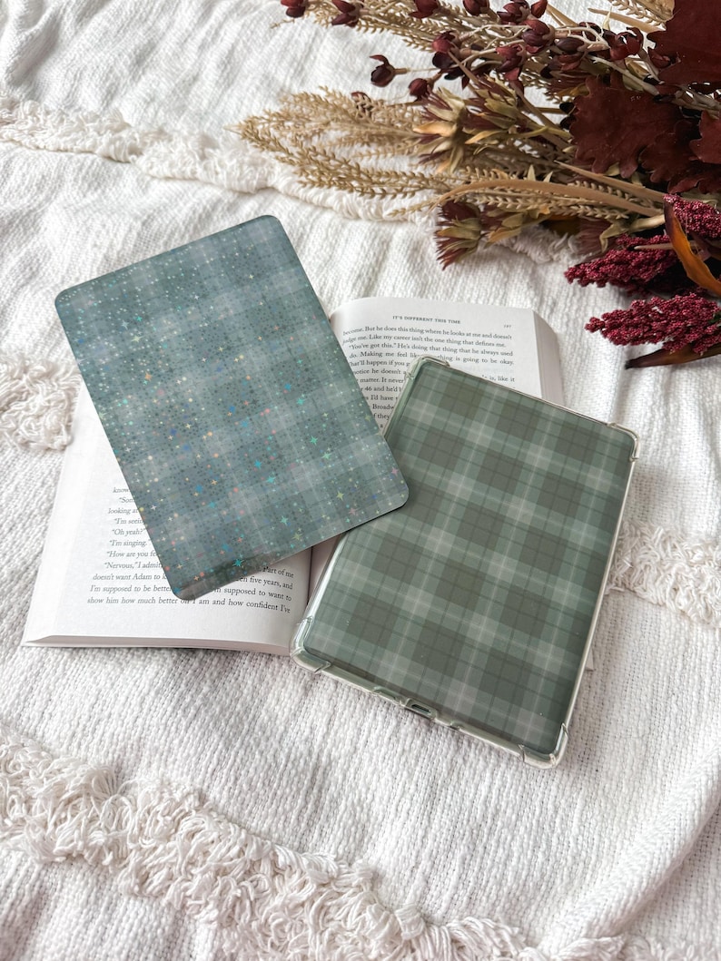 May include: Two rectangular e-reader cases featuring distinct patterns. One case displays a teal background with a subtle grid of small, shimmering holographic stars. The second case features a muted sage green and gray plaid tartan pattern.