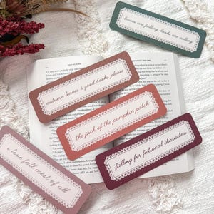 May include: Five rectangular bookmarks with white lace-style borders and cursive text. The bookmarks feature phrases: leaves are falling books are calling, autumn leaves & good books, please, the pick of the pumpkin patch, falling for fictional characters, and i love fall most of all.
