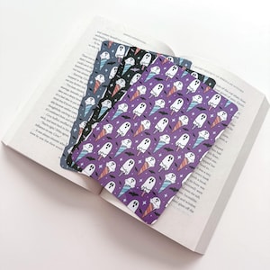 May include: Three rectangular bookmarks featuring a repeating pattern of white ghosts inside ice cream cones, small black bats, and tiny white stars. The bookmarks have purple, black, and dark blue backgrounds, each displaying the same ghost motif.
