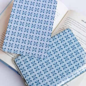 May include: Two blue patterned book covers with a floral design are displayed open on a book. The covers have a clear plastic sleeve. The book pages are visible, with text and a bookmark.