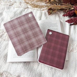May include: Two square acrylic keychains featuring a plaid pattern. One keychain is a light mauve with a darker mauve grid, and the other is a deep burgundy with a dark grid. Each piece has a small circular hole in the corner for attachment.