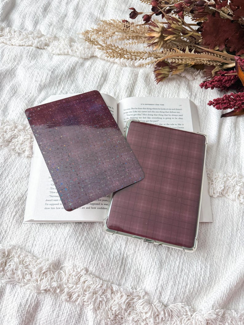 May include: Two rectangular e-reader or tablet cases. One case features a dark purple surface with a fine, multi-colored glitter finish. The second case is encased in a clear protective shell and displays a dark maroon and black plaid pattern.