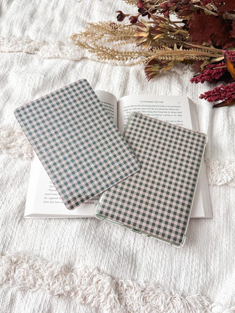 May include: Two rectangular e-reader cases featuring a black and light pink gingham check pattern. One case is positioned flat, while the other is slightly angled, both displaying a consistent grid design across their surfaces.