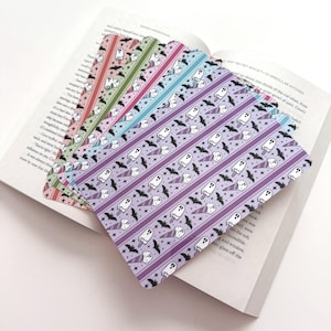 May include: A set of five rectangular bookmarks with rounded corners, each featuring a repeating pattern of white ghosts in ice cream cones and black bats on a background of stars. The bookmarks are layered in shades of purple, blue, green, and pink.
