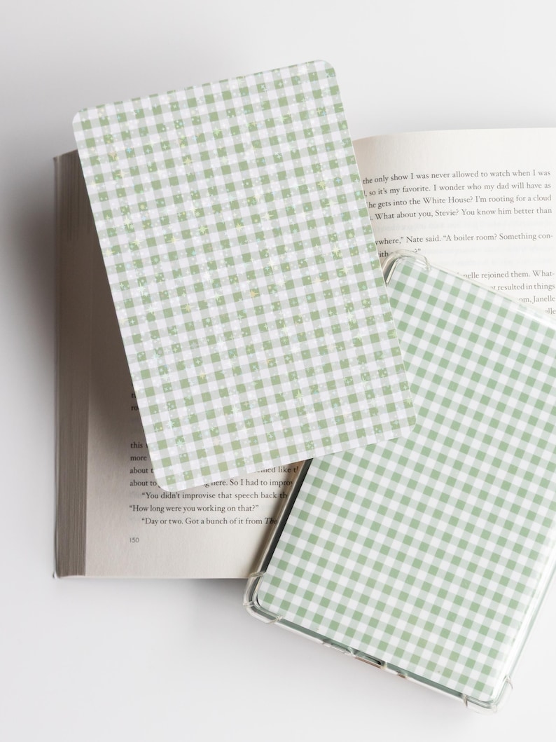 May include: A green and white gingham patterned phone case and a matching card are displayed open on a book. The phone case is clear with a green and white checkered design. The card has the same pattern.