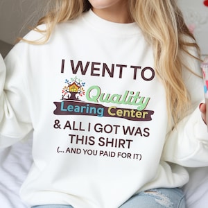 Könnte beinhalten: Weißes Sweatshirt mit dem Text "I WENT TO Quality Learing Center & ALL I GOT WAS THIS SHIRT (...AND YOU PAID FOR IT)". Die Grafik enthält ein Baumhaus-Design und farbigen Text.