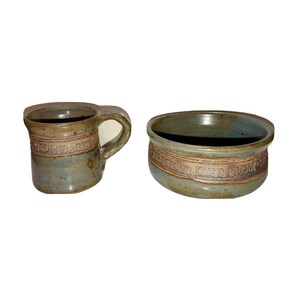 May include: A set of two handmade pottery pieces, a mug and a bowl, both with a blue and brown glaze. The mug has the words "For Baby" inscribed on it, and the bowl has the words "Precious Gift From Heaven" inscribed on it.