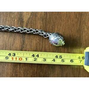 K&ouml;nnte beinhalten: Ein silbernes Kettenarmband mit einem silbernen Anh&auml;nger mit einem filigranen Blumenmuster. Das Armband wird mit einem Ma&szlig;band gemessen und zeigt eine L&auml;nge von 45 Zoll.