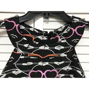 Puede incluir: Vestido negro sin mangas con un patr&oacute;n bordado blanco, rosa y naranja de gafas y corazones. El vestido tiene una cremallera en la espalda.