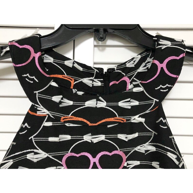 Puede incluir: Vestido negro sin mangas con un patr&oacute;n bordado blanco, rosa y naranja de gafas y corazones. El vestido tiene una cremallera en la espalda.