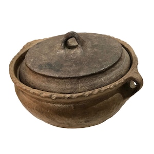 May include: A brown earthenware pot with a lid and a handle. The pot has a rough, textured surface and a slightly rounded shape.