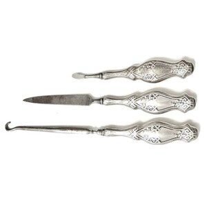 May include: A set of three silver-toned tools with ornate handles. The tools include a hook, a nail file, and a cuticle pusher.