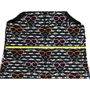 Puede incluir: Tela negra con un patr&oacute;n repetido de flechas blancas y caras estilizadas que llevan gafas de sol. Las gafas de sol son rosas, naranjas y en forma de coraz&oacute;n.