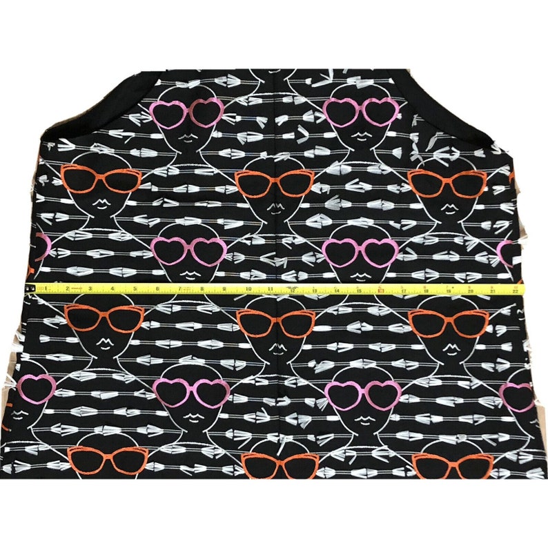 Puede incluir: Tela negra con un patr&oacute;n repetido de flechas blancas y caras estilizadas que llevan gafas de sol. Las gafas de sol son rosas, naranjas y en forma de coraz&oacute;n.