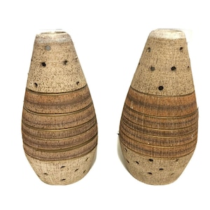 May include: A pair of brown and beige ceramic vases with gold accents and a textured surface. The vases have a rounded, teardrop shape with holes throughout the surface.