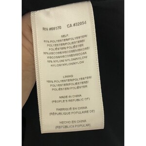 Puede incluir: Una etiqueta de cuidado blanca con texto negro que detalla la composici&oacute;n de la tela y el origen de la prenda. La etiqueta dice "RN #68170 CA #32054", "SELF", "60% POLYESTER/POLYESTER/POLYESTERIPOLIESTERE POLI&Eacute;STER/POLIESTER", "30% VISCOSE/VISCOSEVISKOSE VISCOSAVISCOSEMISCOSA", "10% NYLON/ NYLON/NYLONI NYLONI NYLONINYLON", "LINING: 100% POLYESTER/POLYESTERI POLYESTER/POLIESTERE/ POLI&Eacute;STERI POLI&Eacute;STER", "MADE IN CHINA (PEOPLE'S REPUBLIC OF)", "FABRIQU&Eacute; EN CHINA (R&Eacute;PUBLIQUE POPULAIRE DE)", "HECHO EN CHINA (REP&Uacute;BLICA POPULAR)".