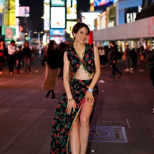 以下が含まれることがあります： Vネックのノースリーブクロップドトップスと、深いスリットが入ったお揃いのマキシスカートのツーピースセット。どちらも黒地に赤、緑、青の鮮やかな花柄が施されており、縁にはゴールドトーンの装飾的なトリムがあしらわれています。