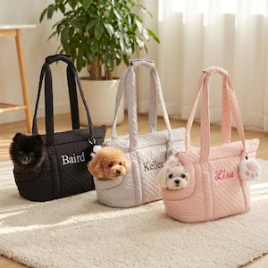 May include: Three quilted pet carrier bags in black, light gray, and light pink. Each bag features a side opening with a small dog inside, long shoulder straps, and personalized embroidery reading Baird, Keller, and Lisa respectively.