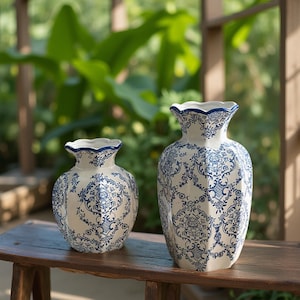 Può includere: Due vasi in ceramica con base bianca e intricati motivi floreali blu. I vasi hanno un bordo smerlato e poggiano su una superficie di legno. Il vaso più grande è alto circa 30 cm, e il vaso più piccolo è alto circa 20 cm.