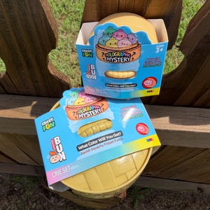 May include: Two boxes of "Crazy Fun Bun Holographic Mystery" fidget toys. The boxes are blue and yellow, with the text "What Color Will You Get?" and "Squish Squashy Fidget Fun!" The toys are for ages 3+.