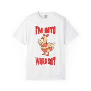 May include: White t-shirt with the text "I'M INTO WEIRD SHIT" in red. The shirt features a cartoon goose wearing a bikini and a bow. The goose is orange and the bikini is pink.