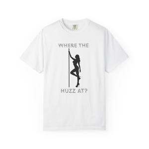 Op de afbeelding: Wit T-shirt met een zwarte afbeelding van een vrouw die paaldanst. De tekst "WHERE THE HUZZ AT?" staat boven en onder de afbeelding. Het shirt heeft een ronde hals.