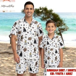 May include: Matching white Hawaiian shirts and shorts featuring Star Wars and Disney characters. The shirts have short sleeves and a button-down design. The outfits are worn by an adult and a child on a beach.