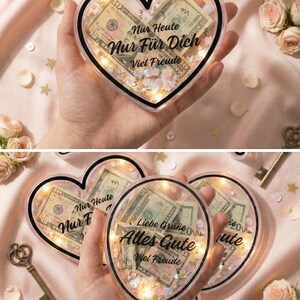 Puede incluir: Caja de regalo acr&iacute;lica transparente en forma de coraz&oacute;n llena de billetes de d&oacute;lar estadounidense, confeti y luces de hadas. El texto "Nur Heute Nur F&uuml;r Dich Viel Freude" es visible. Una idea de regalo rom&aacute;ntica.